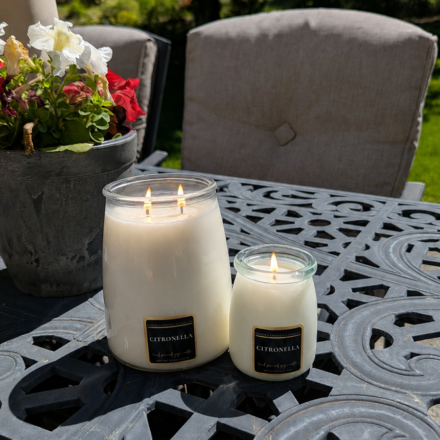 Two citronella candles on a decorative outdoor table with flowers in the background