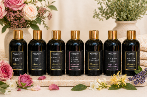 Row of black bottles of diffuser oil fragrances with gold caps on a decorative surface with flowers and plants.