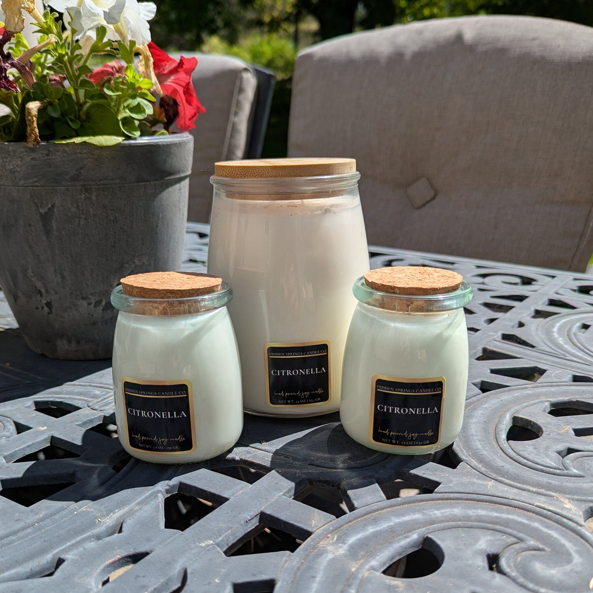 Three citronella candles on a patio table with a potted plant in the background