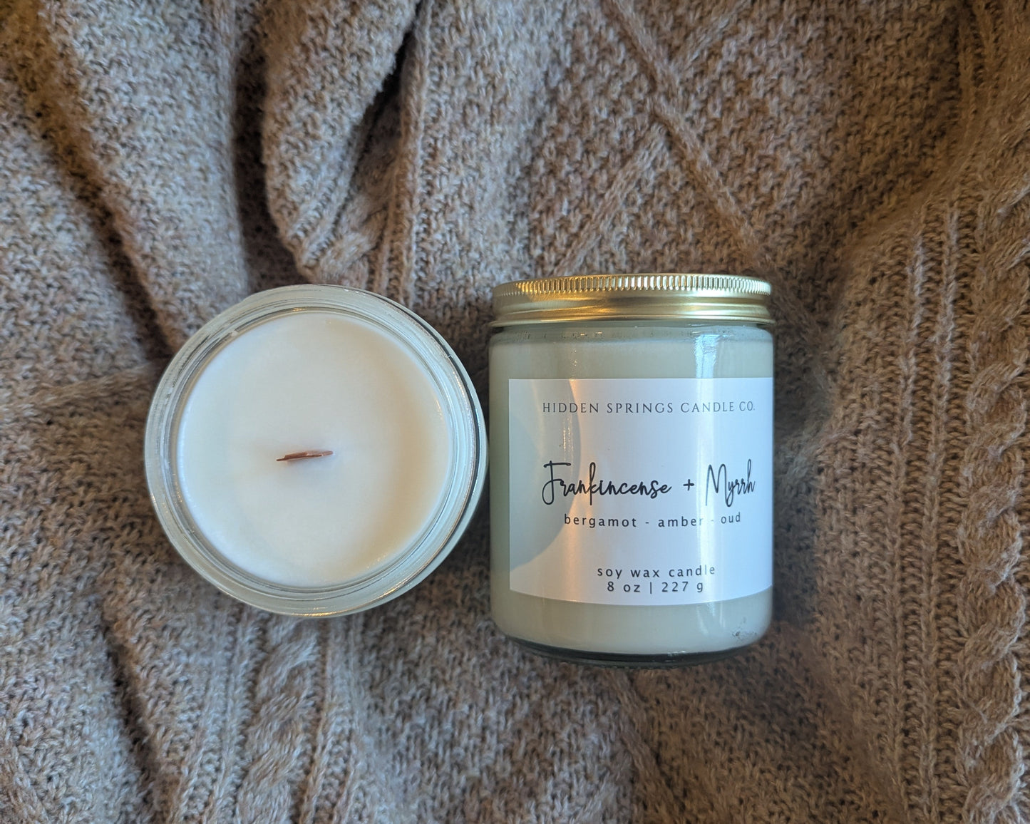 Two candles, one open and one closed, on a textured brown fabric background.