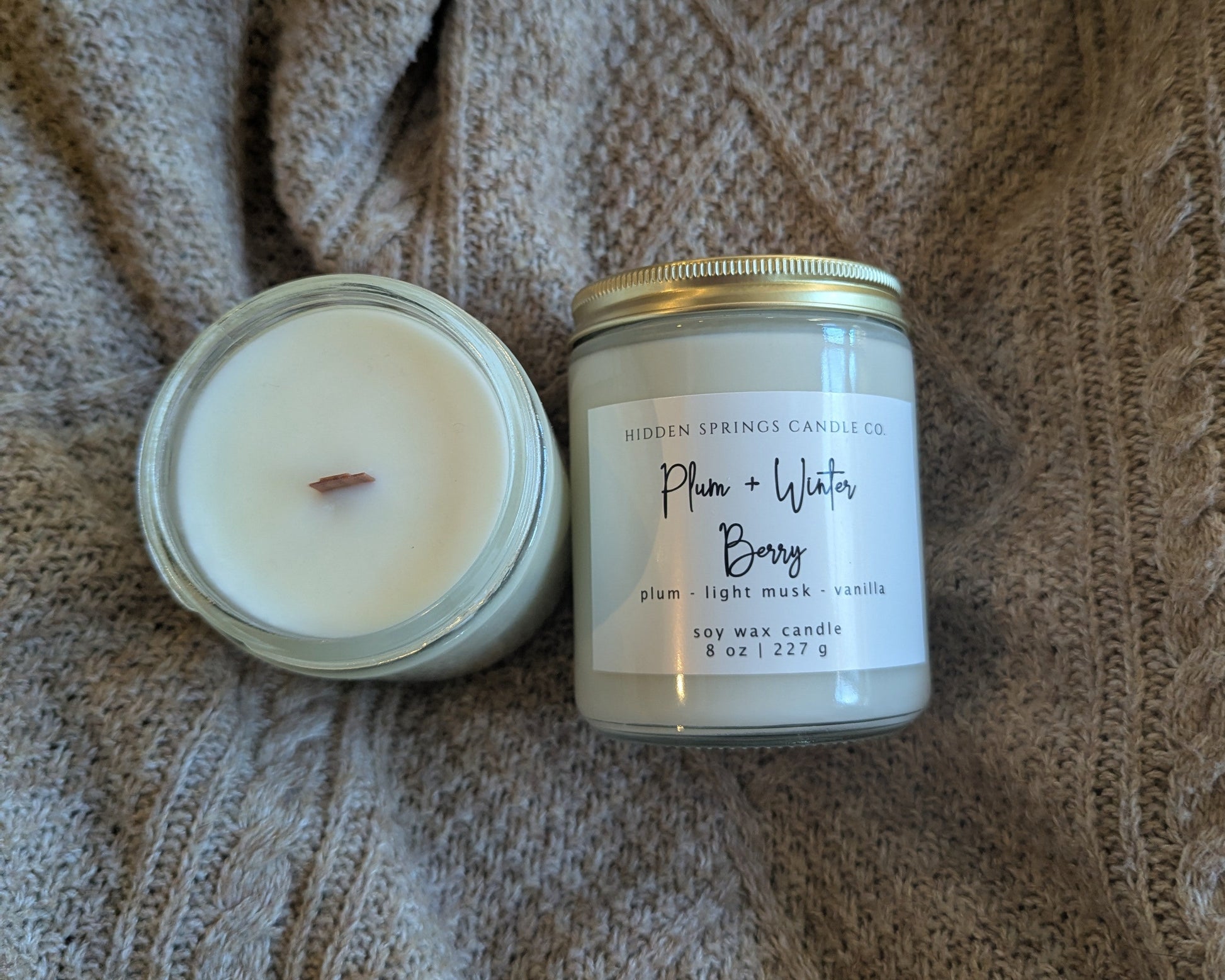 Two crackling wood wick candles on a textured fabric surface