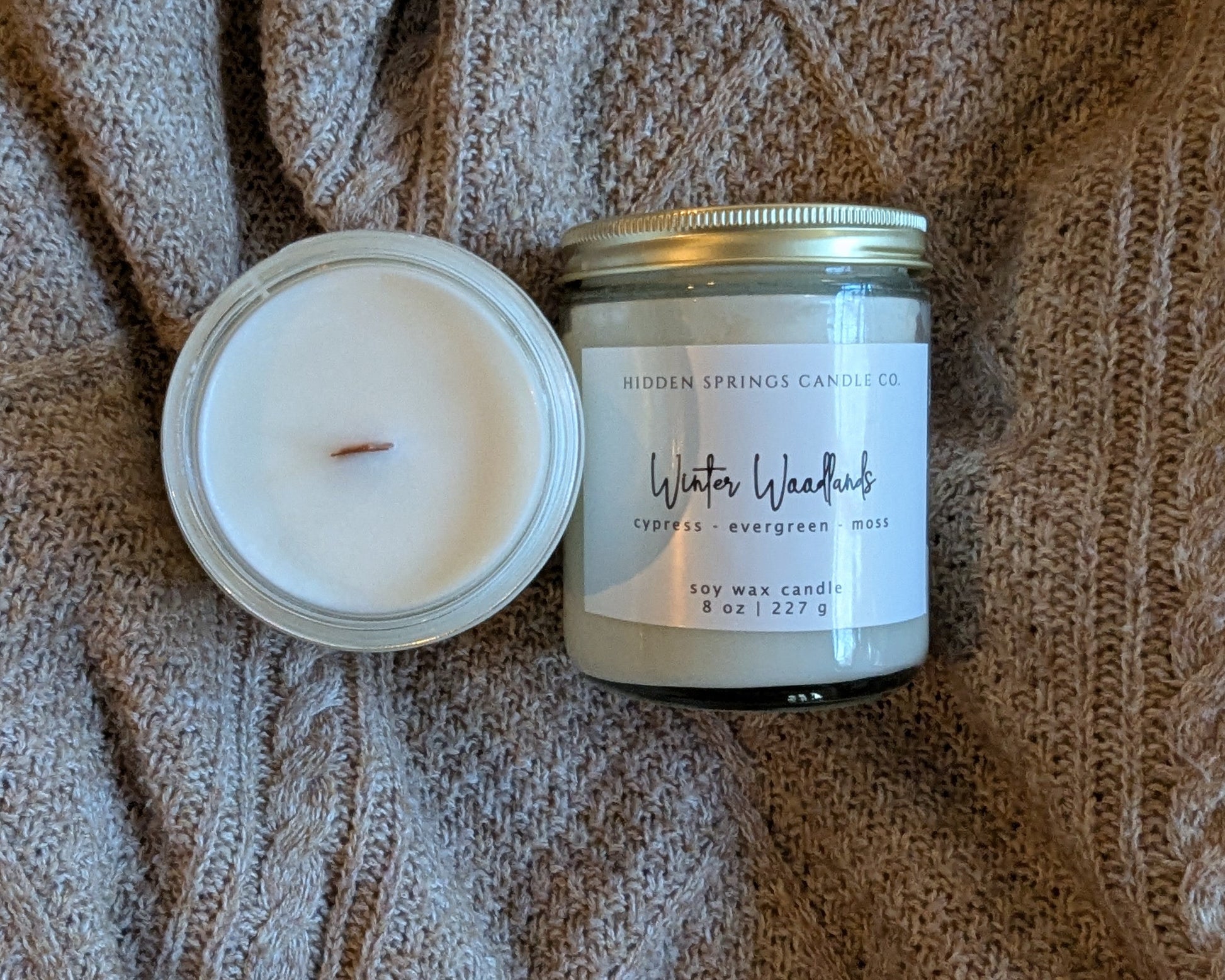 Two crackling wood wick candles on a textured brown fabric background.